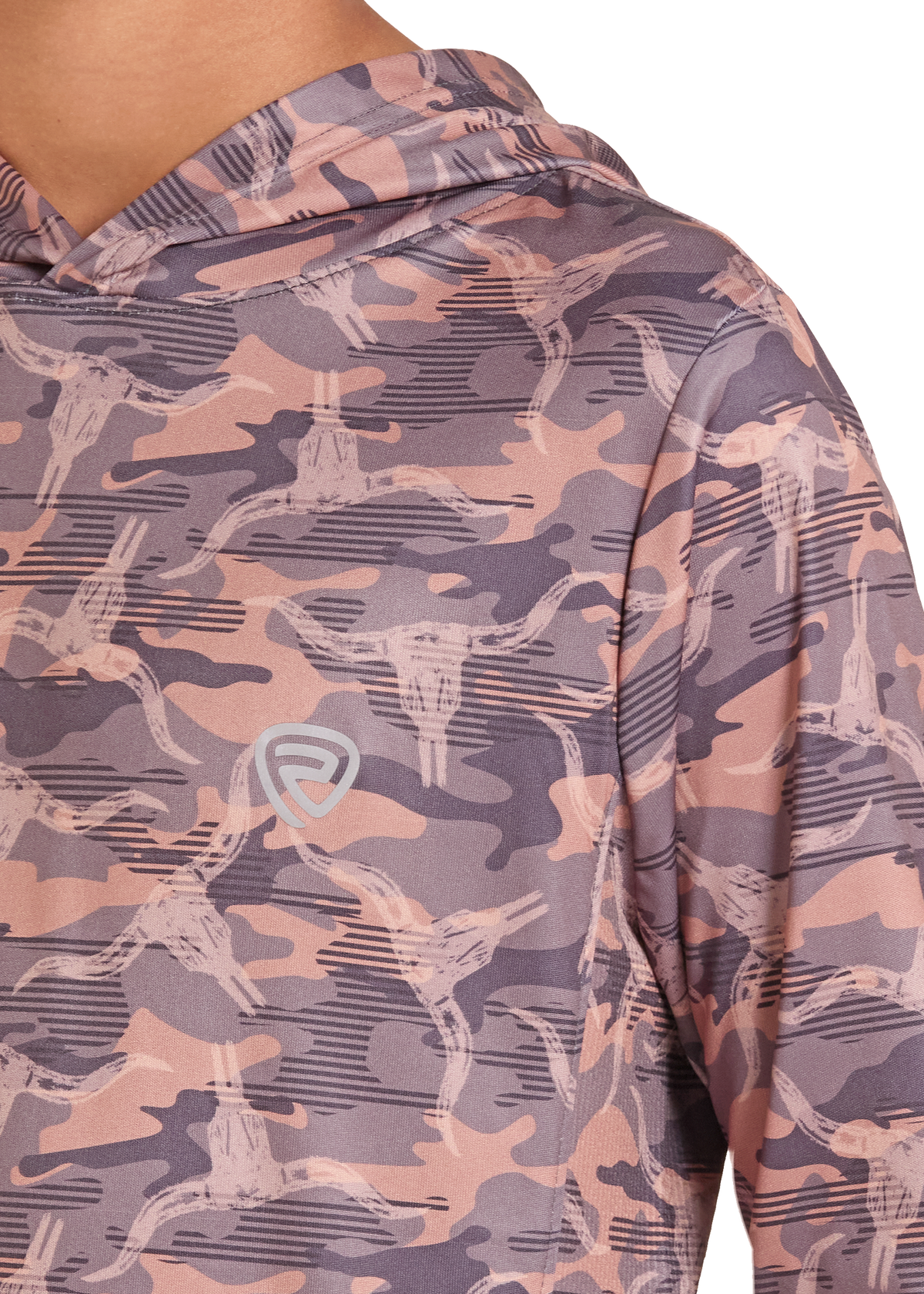 Close-up of a person wearing a hooded long-sleeve shirt with a muted camouflage pattern in dusty pink, mauve, and gray, featuring a stylized bull skull motif and a small shield logo on the chest.