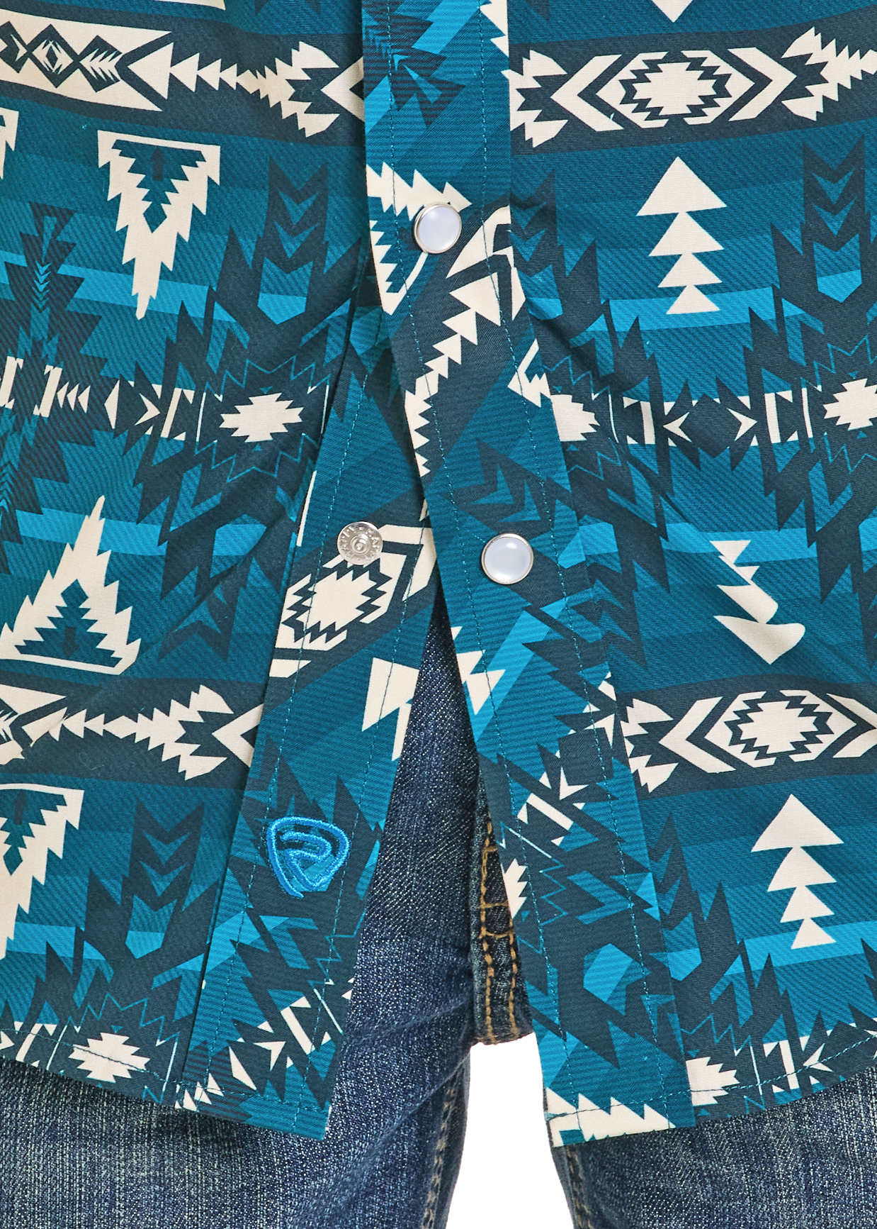 Close-up of the Rock & Roll Denim Boys' Aztec Mountains Long Sleeve Snap Shirt featuring blue and teal geometric patterns, white snaps, and paired with blue denim jeans.
