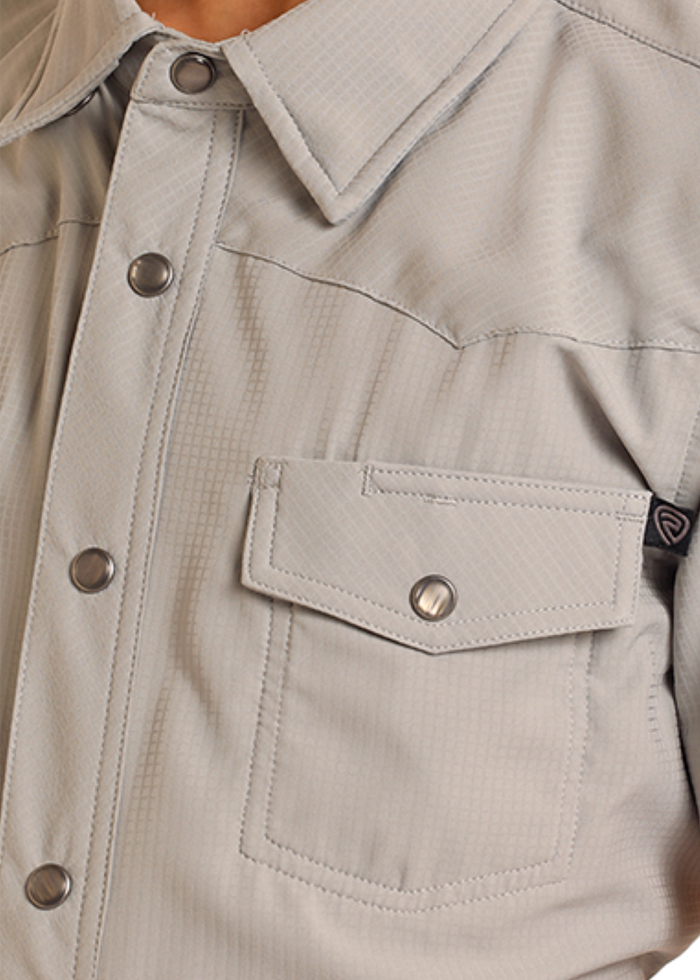 Close-up of a person wearing a light gray short-sleeve shirt with buttons and a pocket.