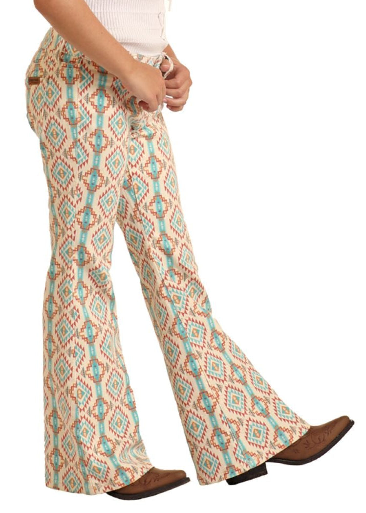 Young girl wearing a white top and patterned bell-bottom pants with a cowboy hat on a white background