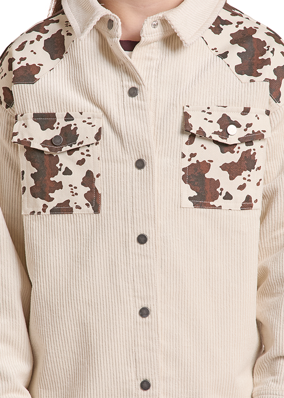 A close-up of a ribbed cream corduroy button-up shirt with brown and beige cow-print panels on the shoulders, chest, and pocket flaps, shown on a model.