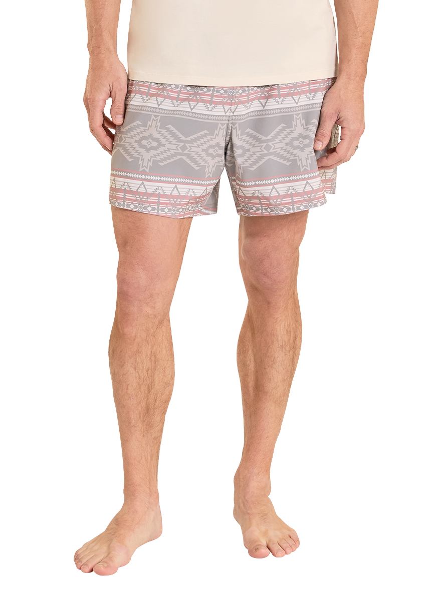 Man wearing a beige t-shirt and patterned shorts on a white background