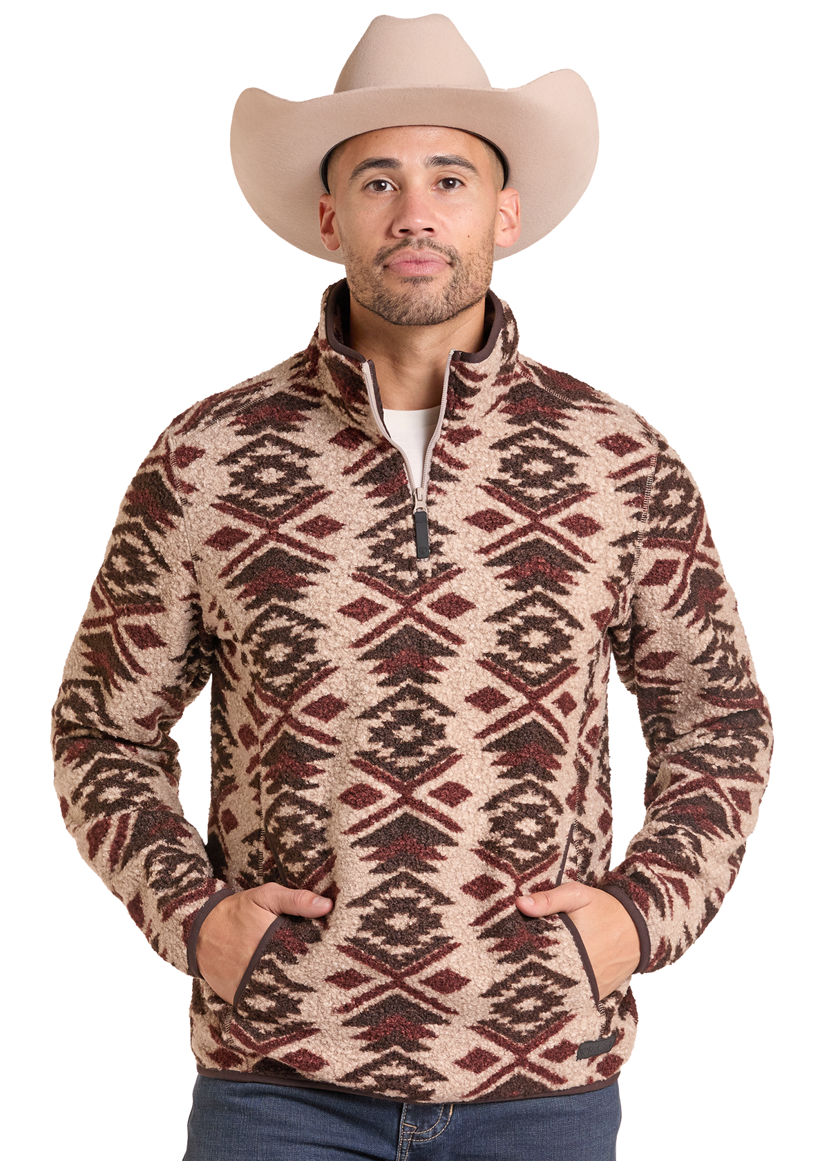 A man wearing a beige cowboy hat and a brown and beige geometric patterned quarter-zip fleece pullover sweater, standing against a solid white background.