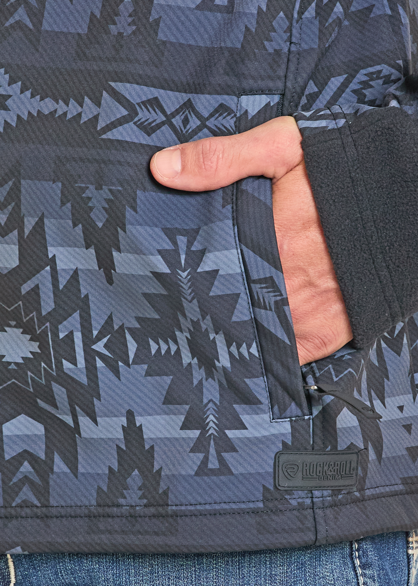 Close-up of a patterned jacket with a hand holding the sleeve, brand logo visible.