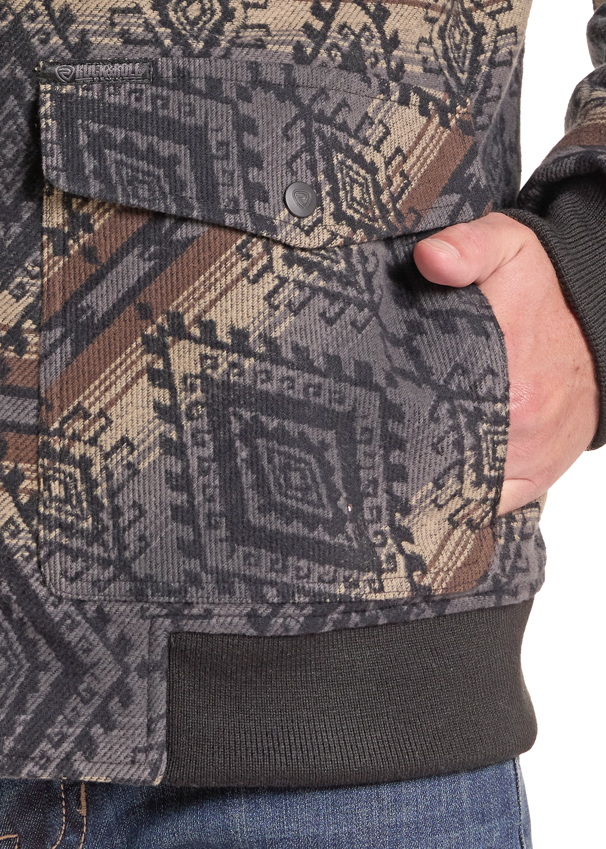 Close-up of a person wearing a patterned jacket with a flap pocket and ribbed cuffs, showing a hand in the pocket against a white background.