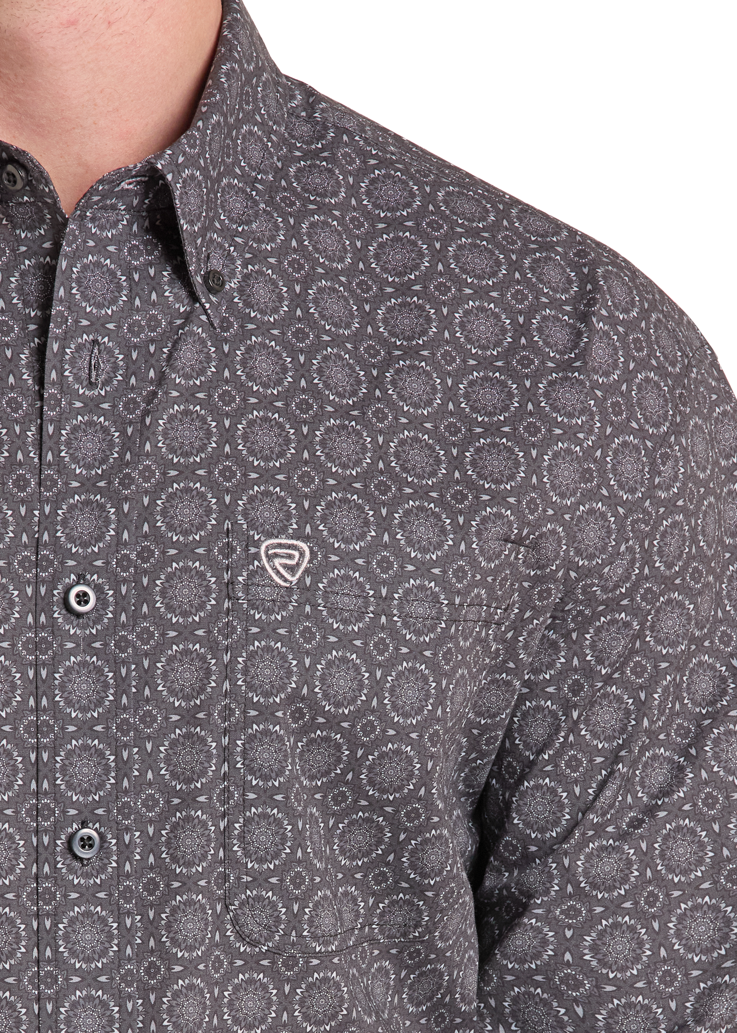 Close-up of a man wearing a dark gray button-down shirt with a circular dot pattern and a small shield logo on the chest pocket.