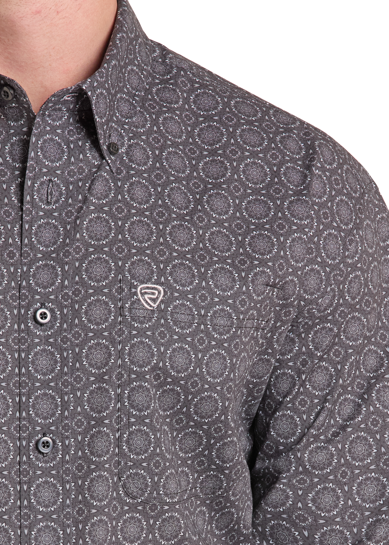 Close-up of a man wearing a dark gray button-down shirt with a circular dot pattern and a small shield logo on the chest pocket.
