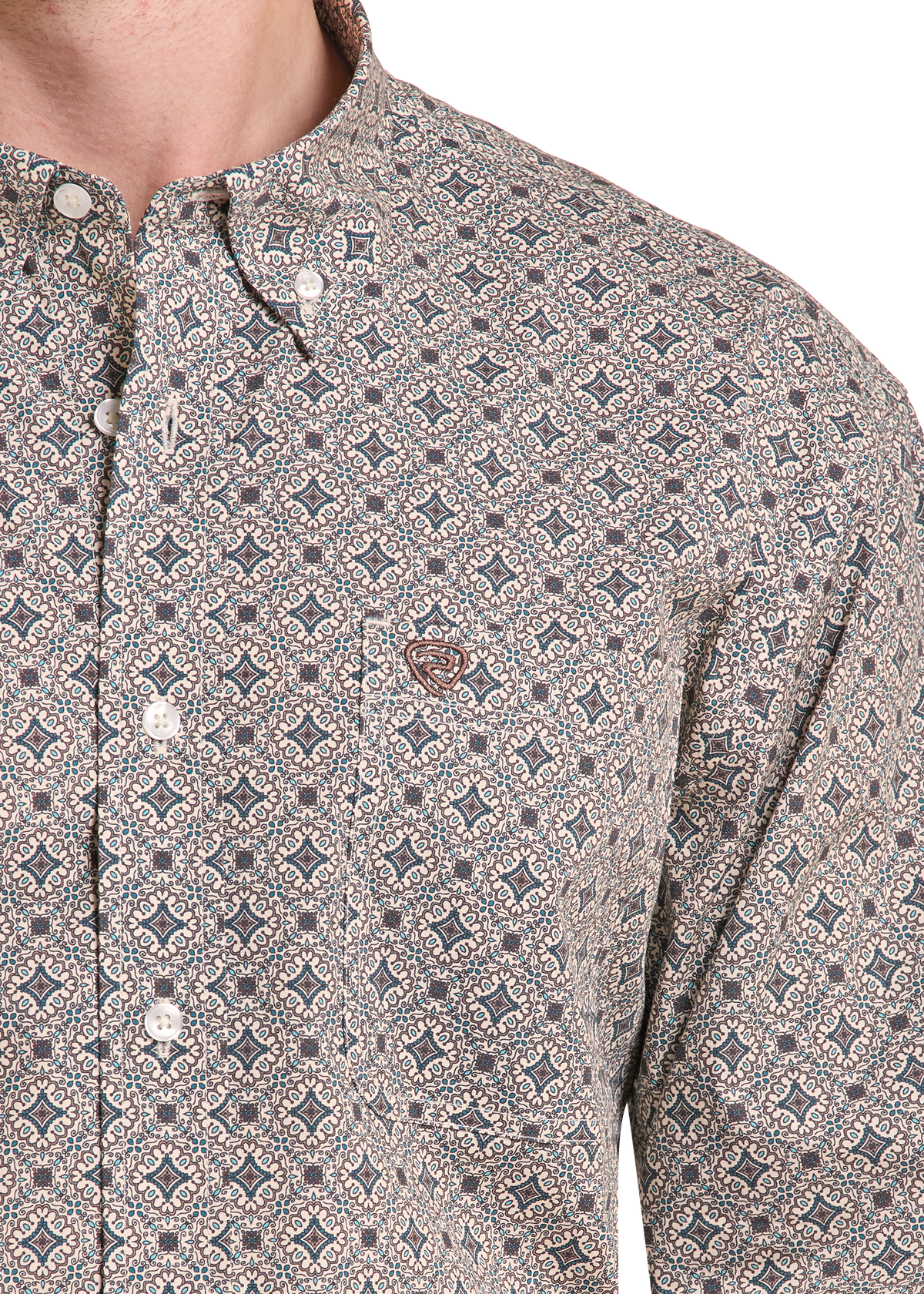 Close-up of a men's button-down shirt with a small-scale geometric pattern in beige, gray, and brown, featuring a chest pocket with a brown embroidered logo.