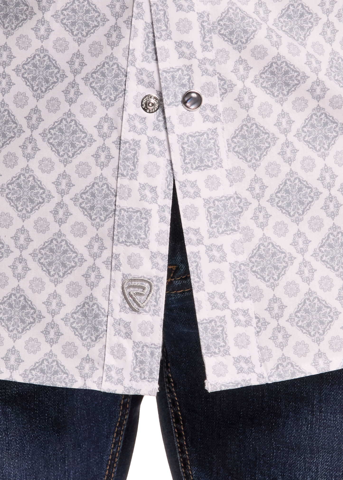 Close-up of a light gray and white patterned button-up shirt worn over dark blue jeans, showing the fabric pattern and a small shield logo patch near the pocket.