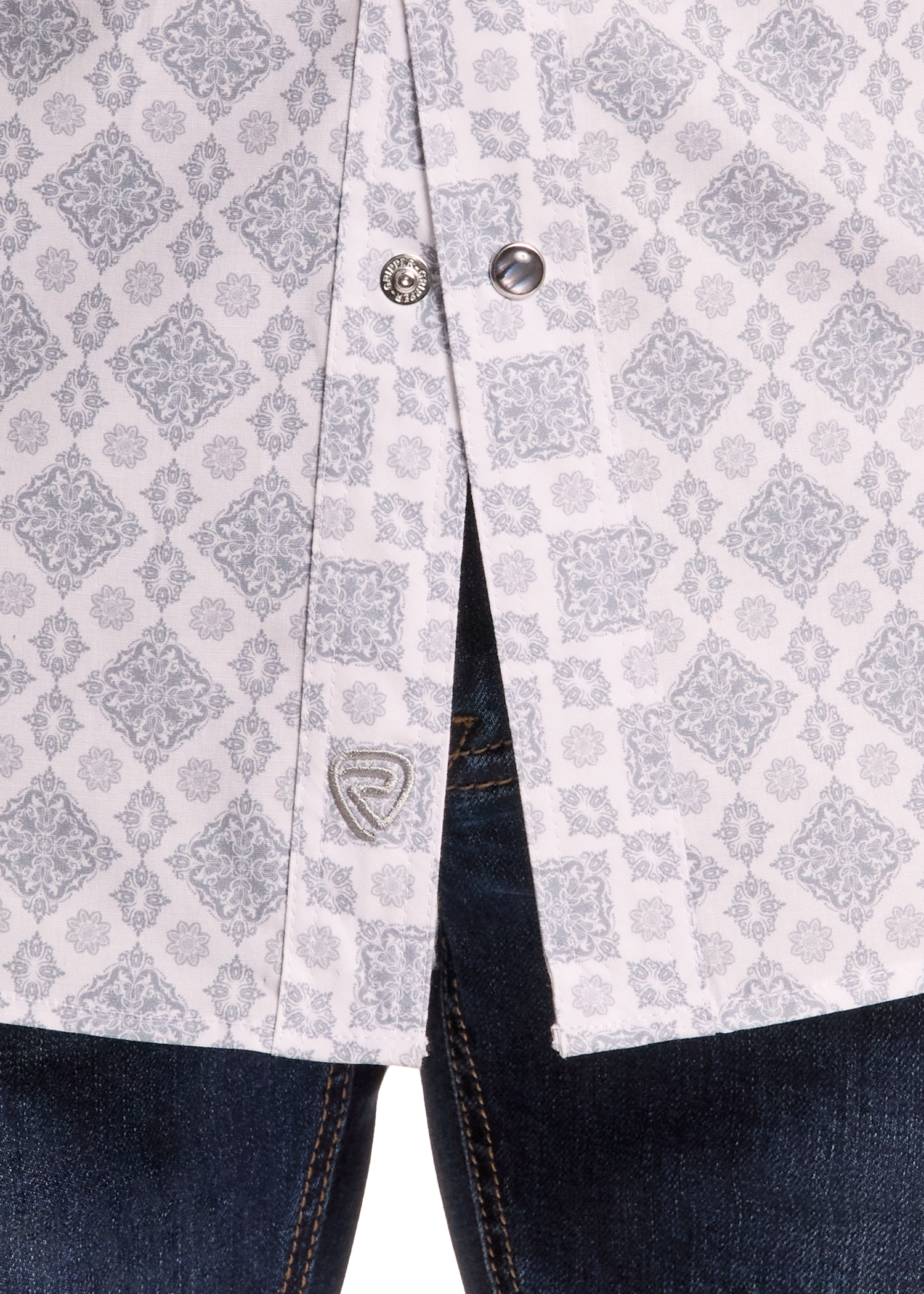 Close-up of a light gray and white patterned button-up shirt worn over dark blue jeans, showing the fabric pattern and a small shield logo patch near the pocket.