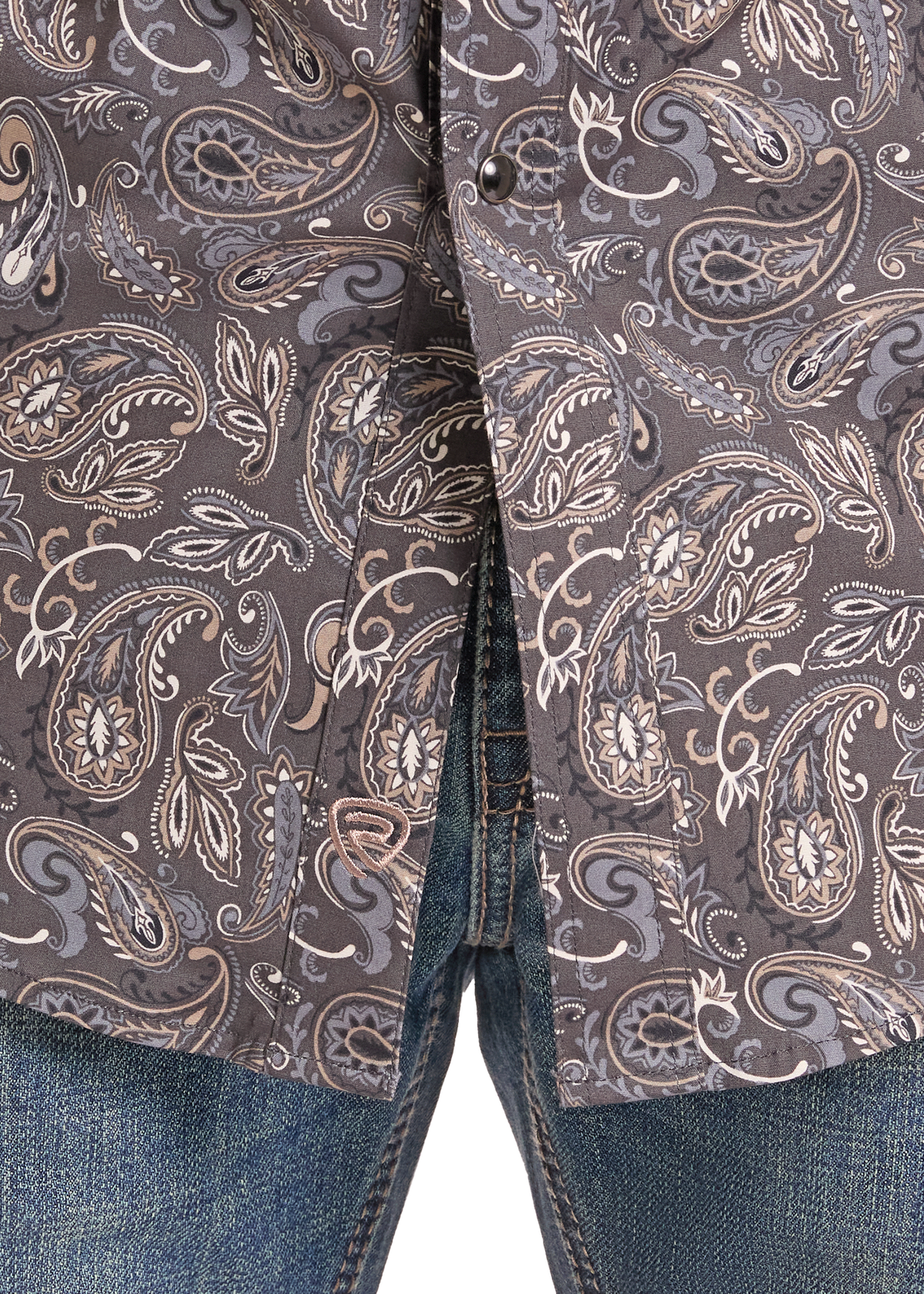 Close-up of a button-front shirt with a brown, gray, and beige paisley pattern, worn with blue jeans.