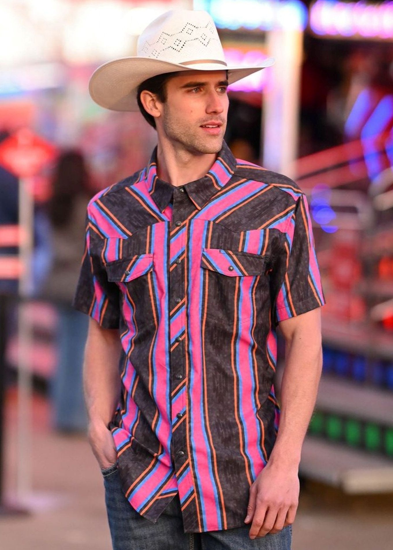 Man wearing a colorful patterned shirt and cowboy hat in an urban setting