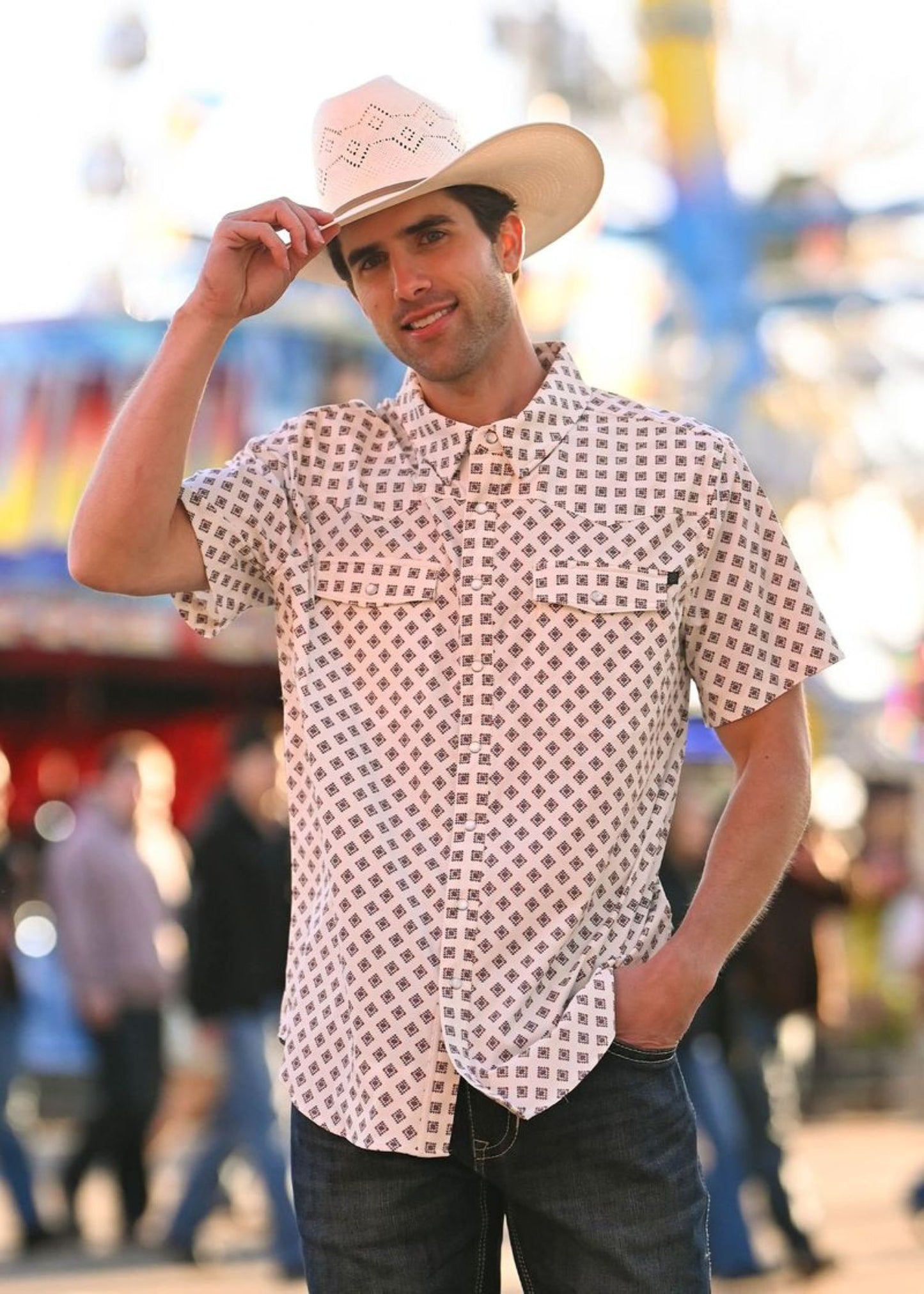 Man wearing a cowboy hat and patterned shirt in an outdoor setting with blurred background