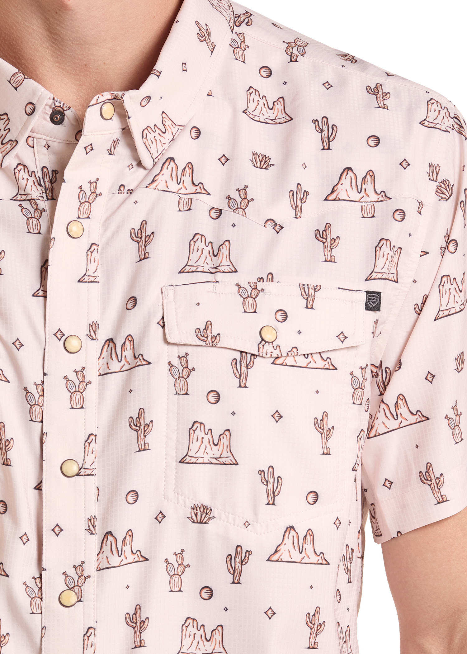 A close-up of a short-sleeve button-up shirt featuring a light pink base with a brown desert cactus and rock pattern, accented by gold-tone snap buttons and a chest pocket.