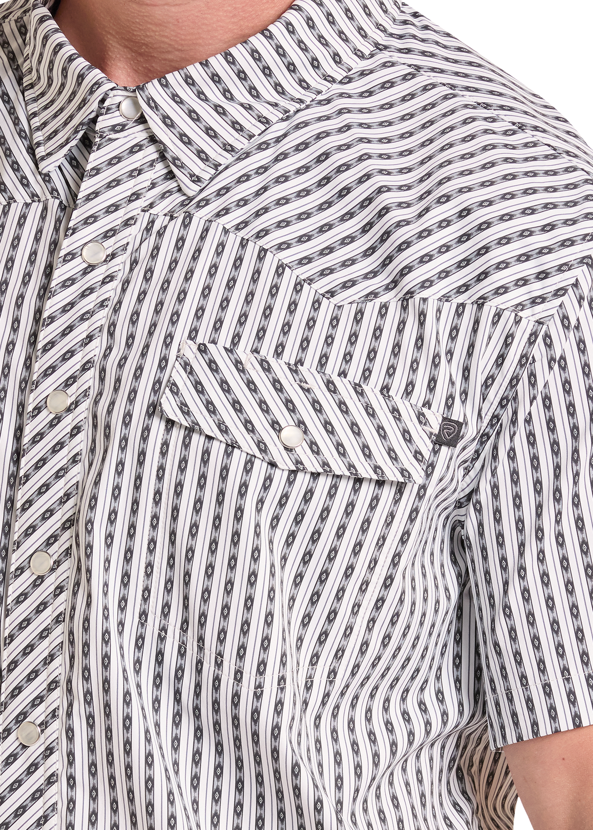 Close-up of a short-sleeve button-up shirt worn by a model, featuring a white base with a repeating black chain-link pattern.