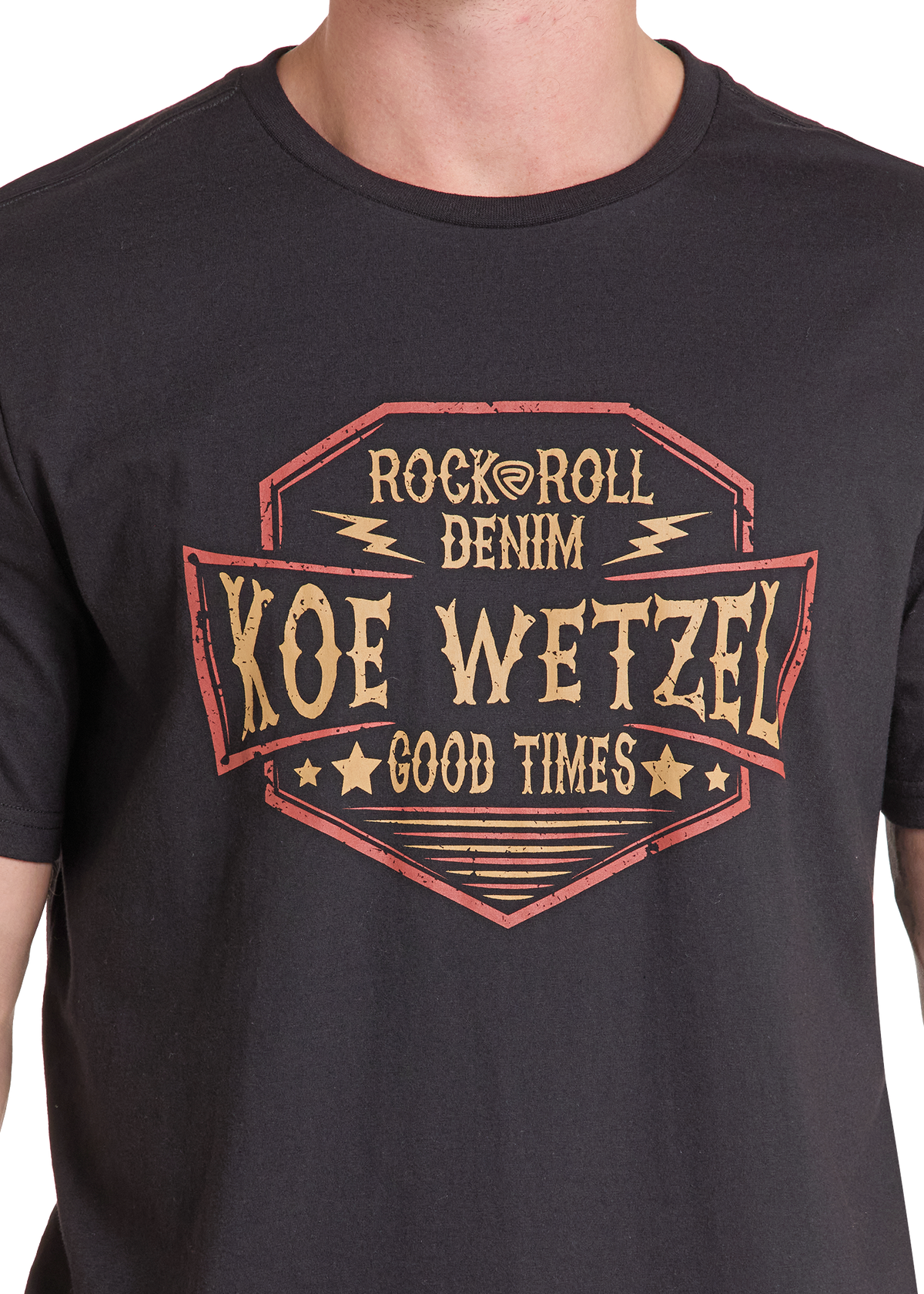 A close-up of a person wearing a black graphic t-shirt. The shirt features a distressed vintage-style badge design in tan and red with the text 'ROCK@ROLL DENIM', 'KOE WETZEL', and 'GOOD TIMES'.