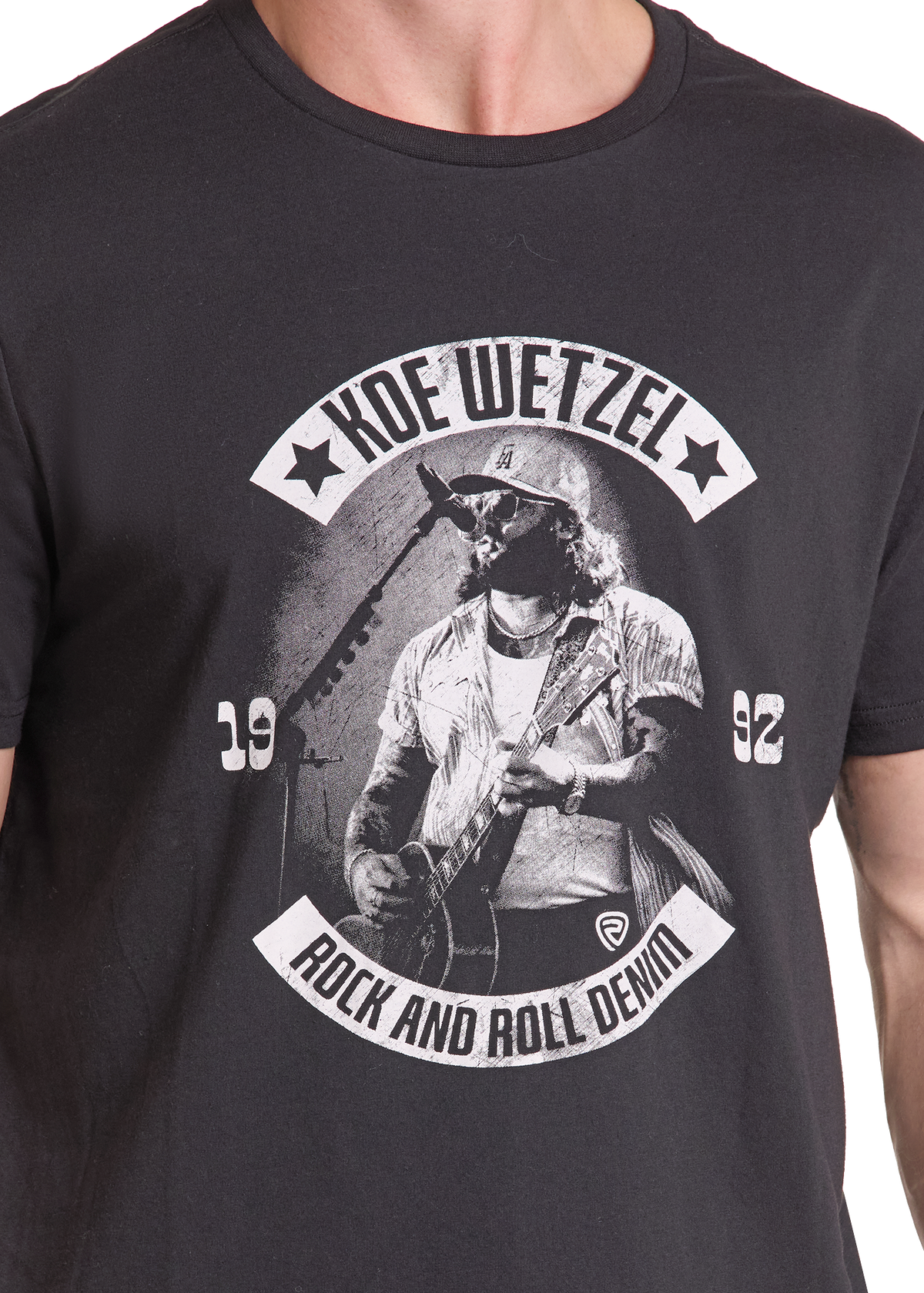 A close-up of a person wearing a black graphic t-shirt. The shirt features a white and gray print of Koe Wetzel, a rock and roll musician, with the text 'KOE WETZEL', 'ROCK AND ROLL DENIM', '1992'.