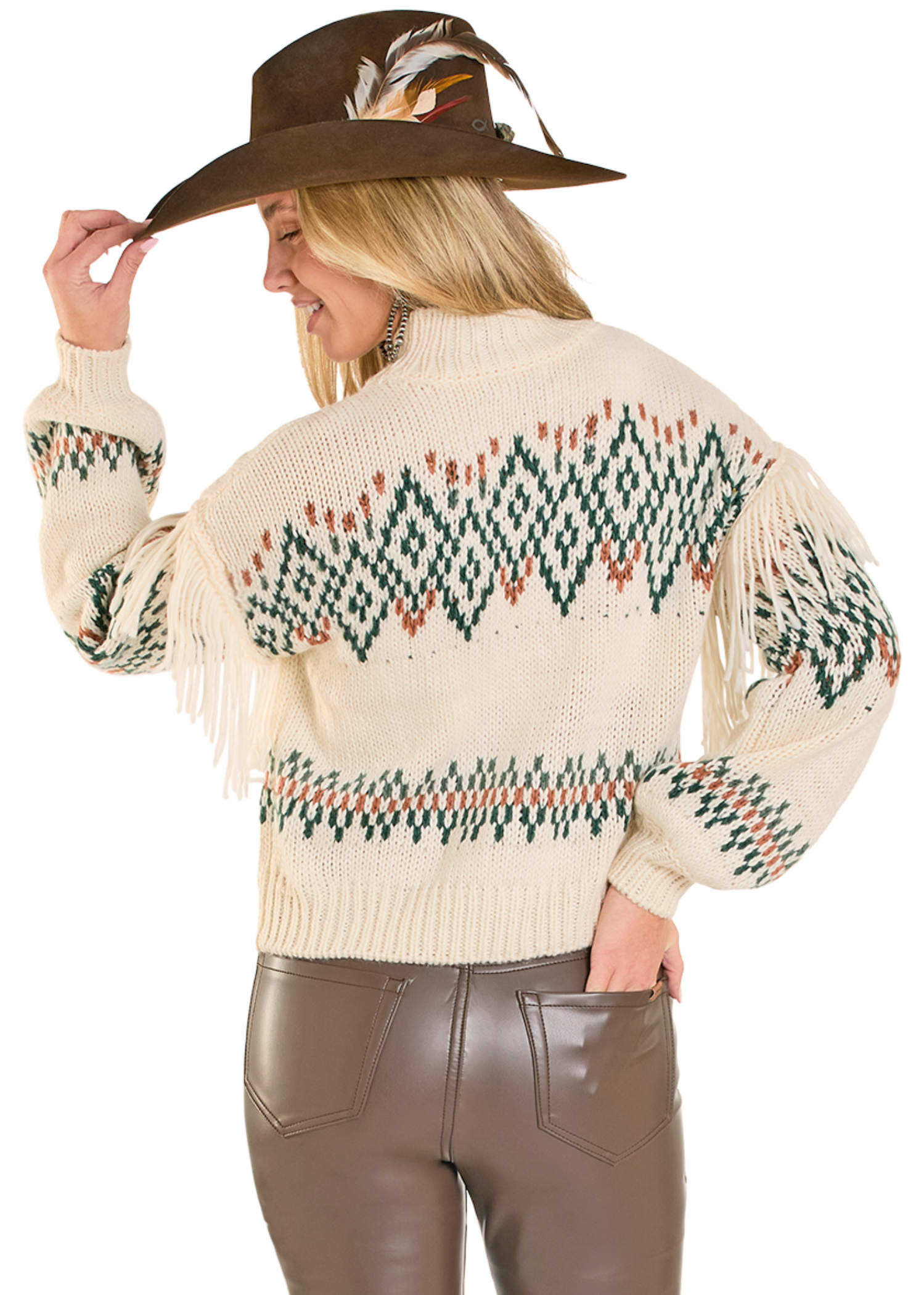Woman wearing a cream-colored sweater with patterned design and fringes, holding a brown hat with feathers.
