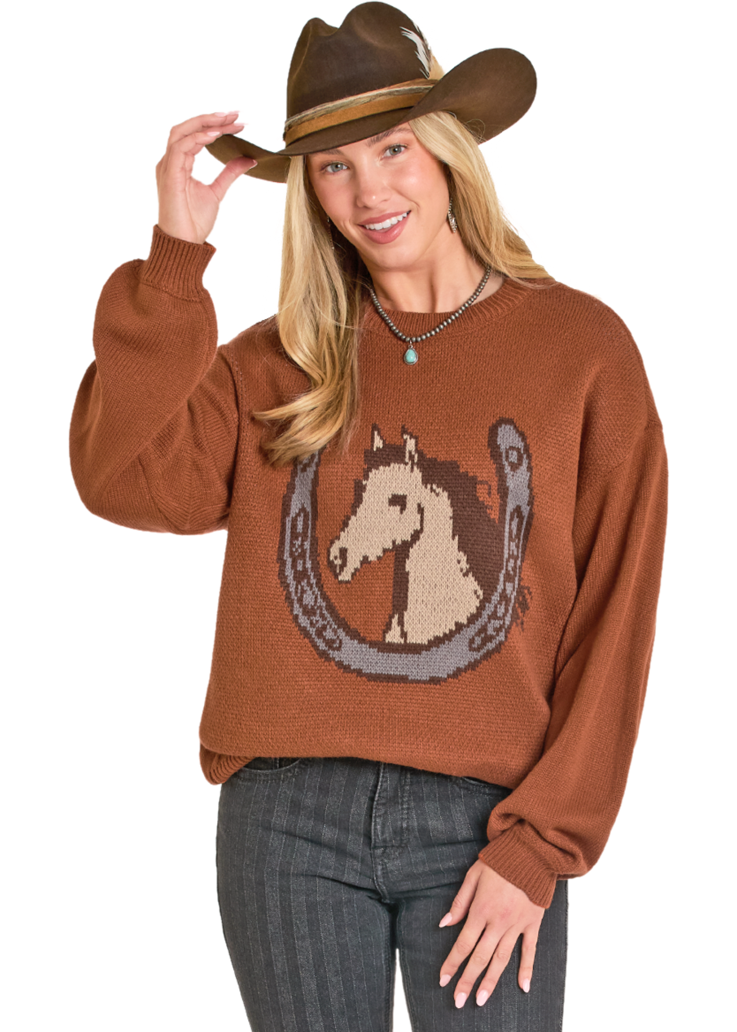 Woman wearing a brown sweater with a horse and horseshoe design, holding a cowboy hat.