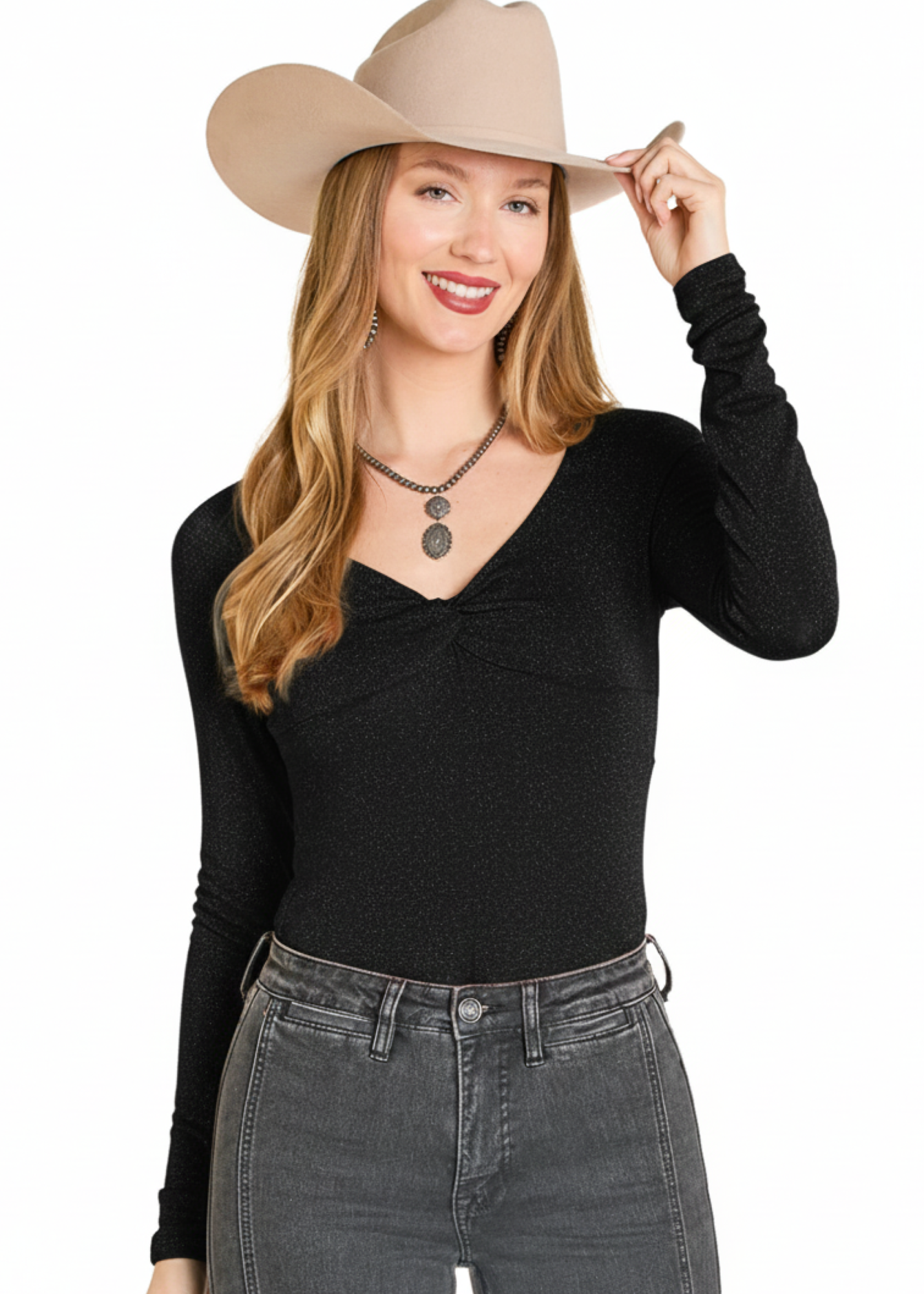 A smiling woman in a beige cowboy hat and Rock & Roll Denim Lurex Long Sleeve Blouse with high-waisted gray jeans stands against a white background, holding her hat brim with one hand.