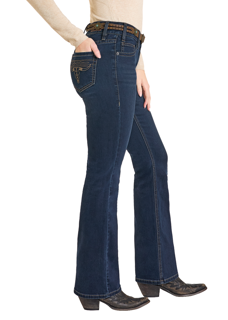 A person stands in a side view with one hand in their pocket, wearing dark blue Rock & Roll Denim Mid Rise Boot Stitch Steer Head Bootcut Jeans, a light long-sleeve top, a brown belt, and black cowboy boots against a white background.