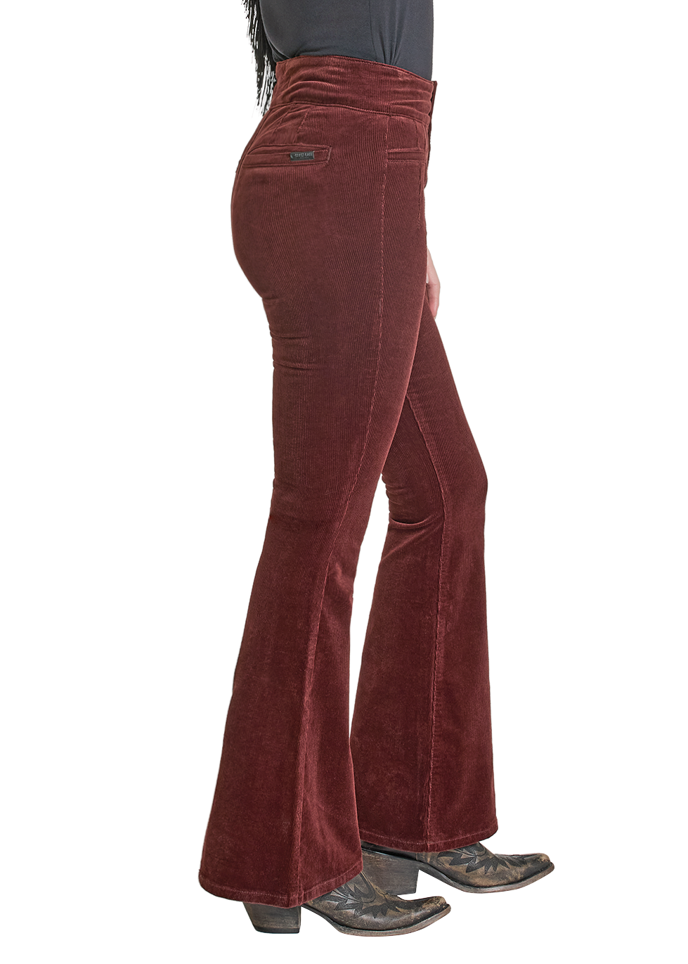 Woman wearing a black top with fringe and brown flared pants, holding a cowboy hat.