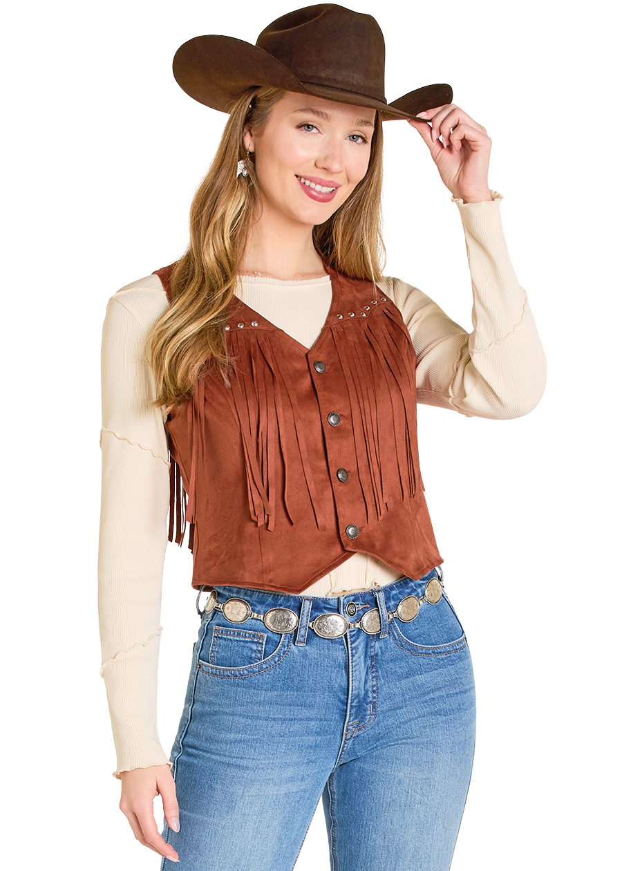 A woman in the Rock & Roll Denim Studded Fringe Microsuede Vest over a cream long-sleeve shirt, with a cowboy hat, silver concho belt, and blue jeans, smiles and tips her hat.