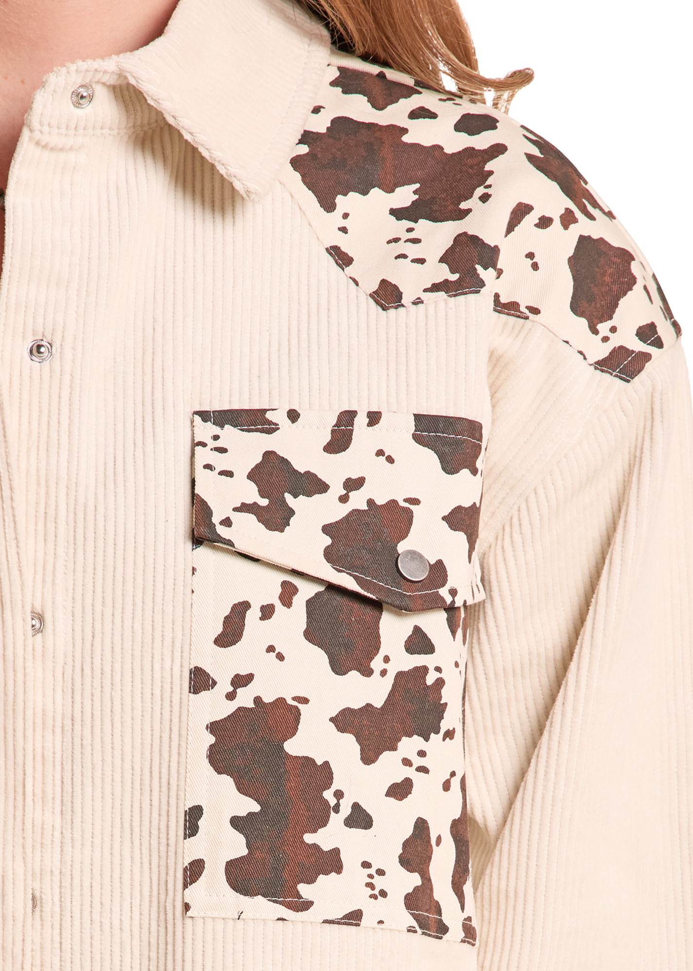 Close-up of a cream ribbed corduroy shirt jacket with brown and cream cow-print patchwork details on the shoulders and chest pocket.