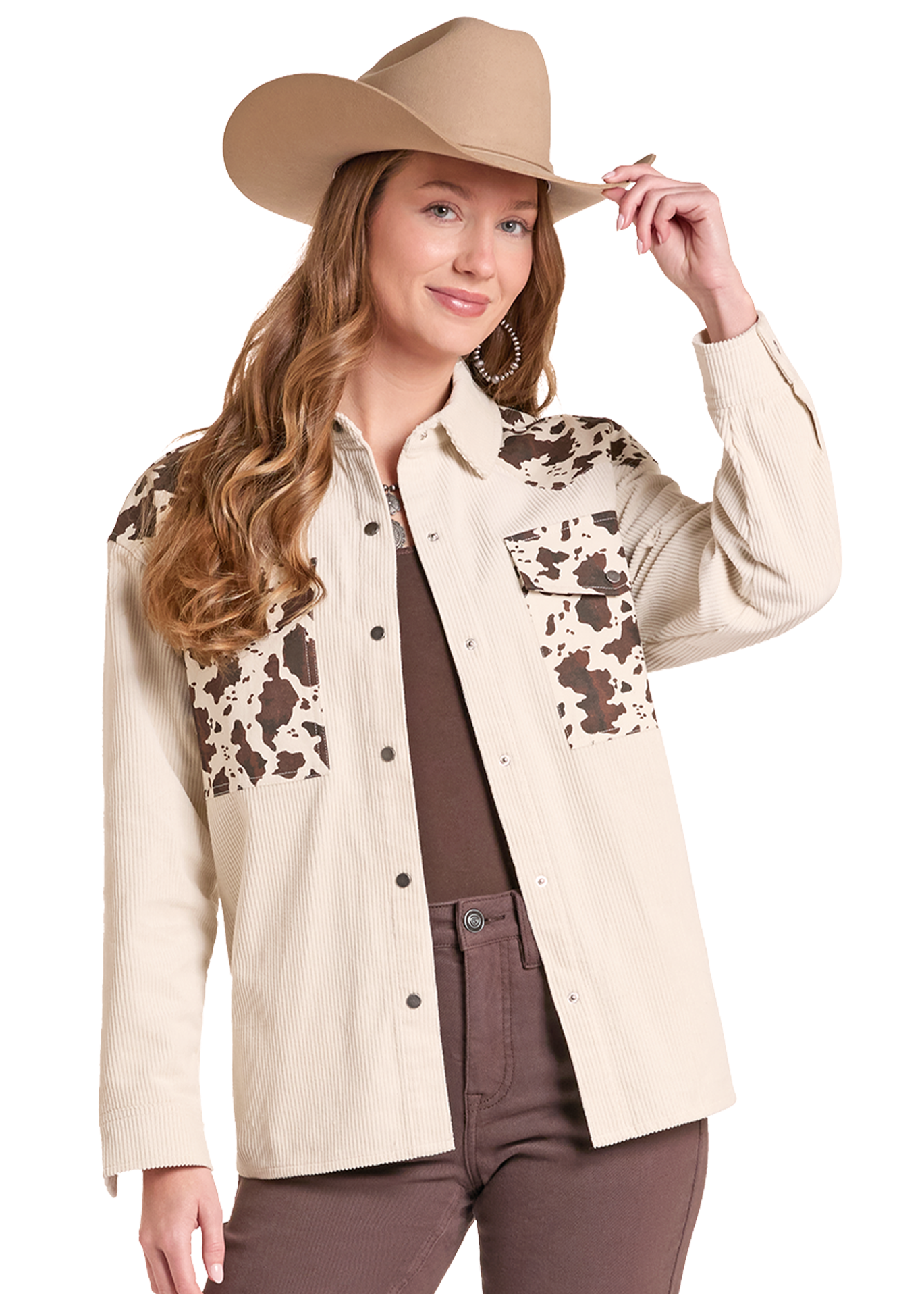 A woman modeling a beige western-style button-up shirt with brown and beige cow-print chest panels, paired with a tan cowboy hat, brown top, and brown pants.