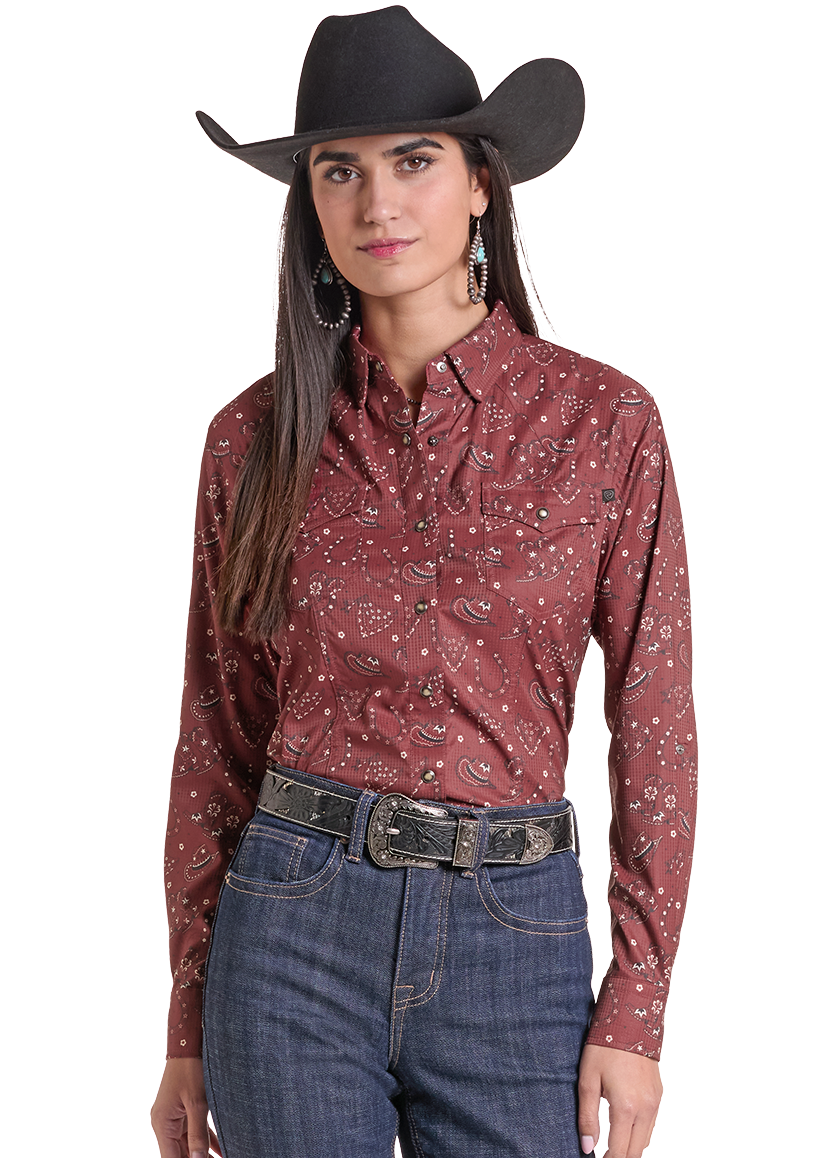 A woman modeling a western-style outfit featuring a rust red long-sleeve button-down shirt with a white floral pattern, dark blue jeans, a black belt, and a black cowboy hat, set against a plain white background.