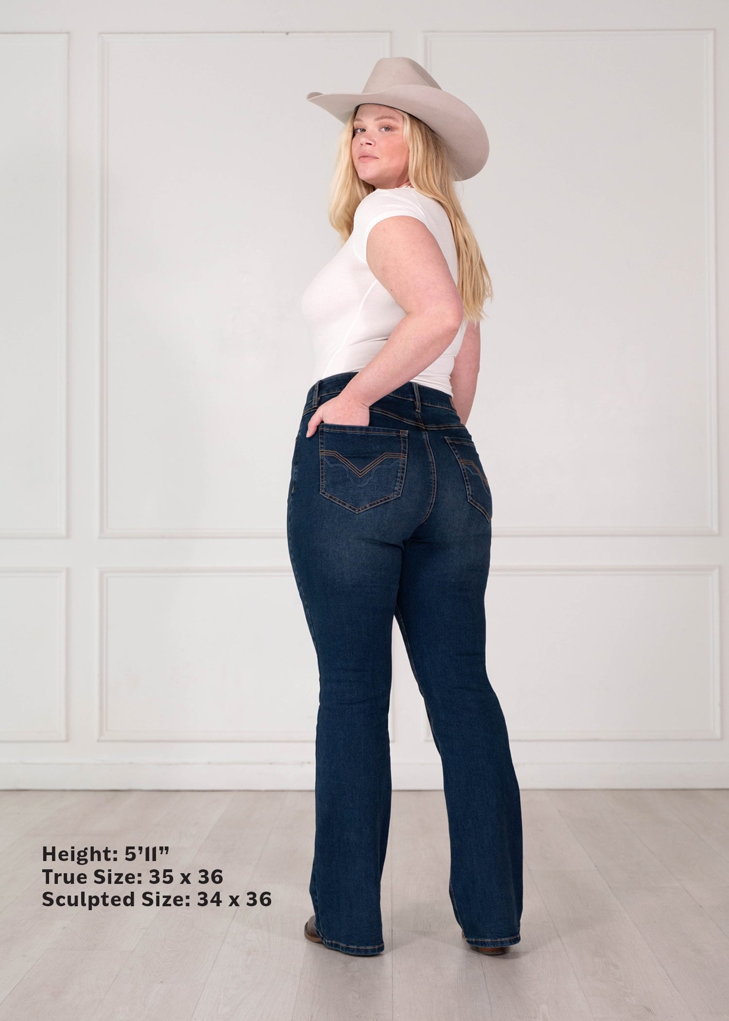 A woman wearing dark blue flared jeans, a white sleeveless top, and a beige cowboy hat, shown from the back in a studio setting with text indicating measurements.