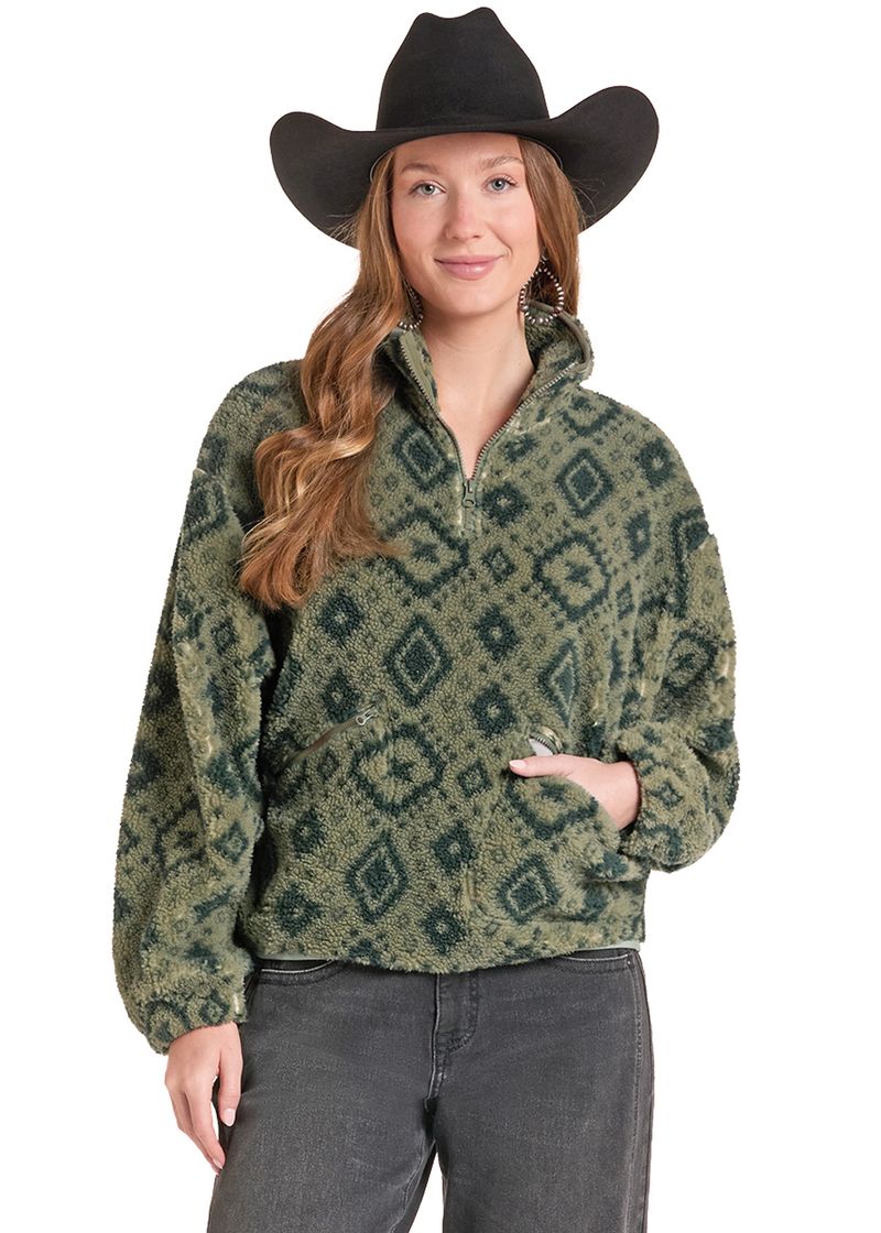 A woman wearing a green and dark green geometric patterned quarter-zip fleece pullover, a black cowboy hat, and dark gray jeans, photographed against a solid white background.