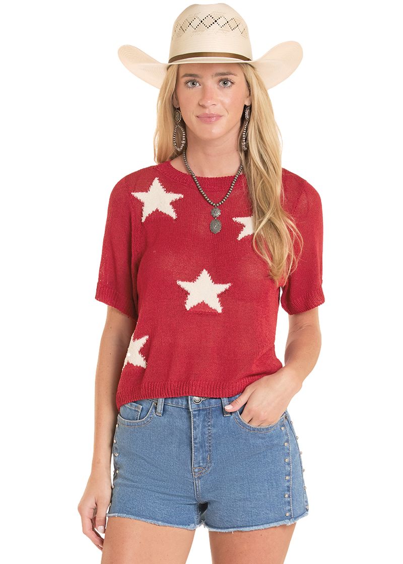 Woman wearing a red sweater with white stars, denim shorts, and a straw hat on a white background