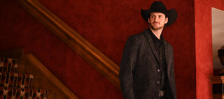 Man in a cowboy hat and suit standing on a staircase with red walls.
