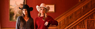 Two women standing on a staircase with ornate wooden railings and red walls.