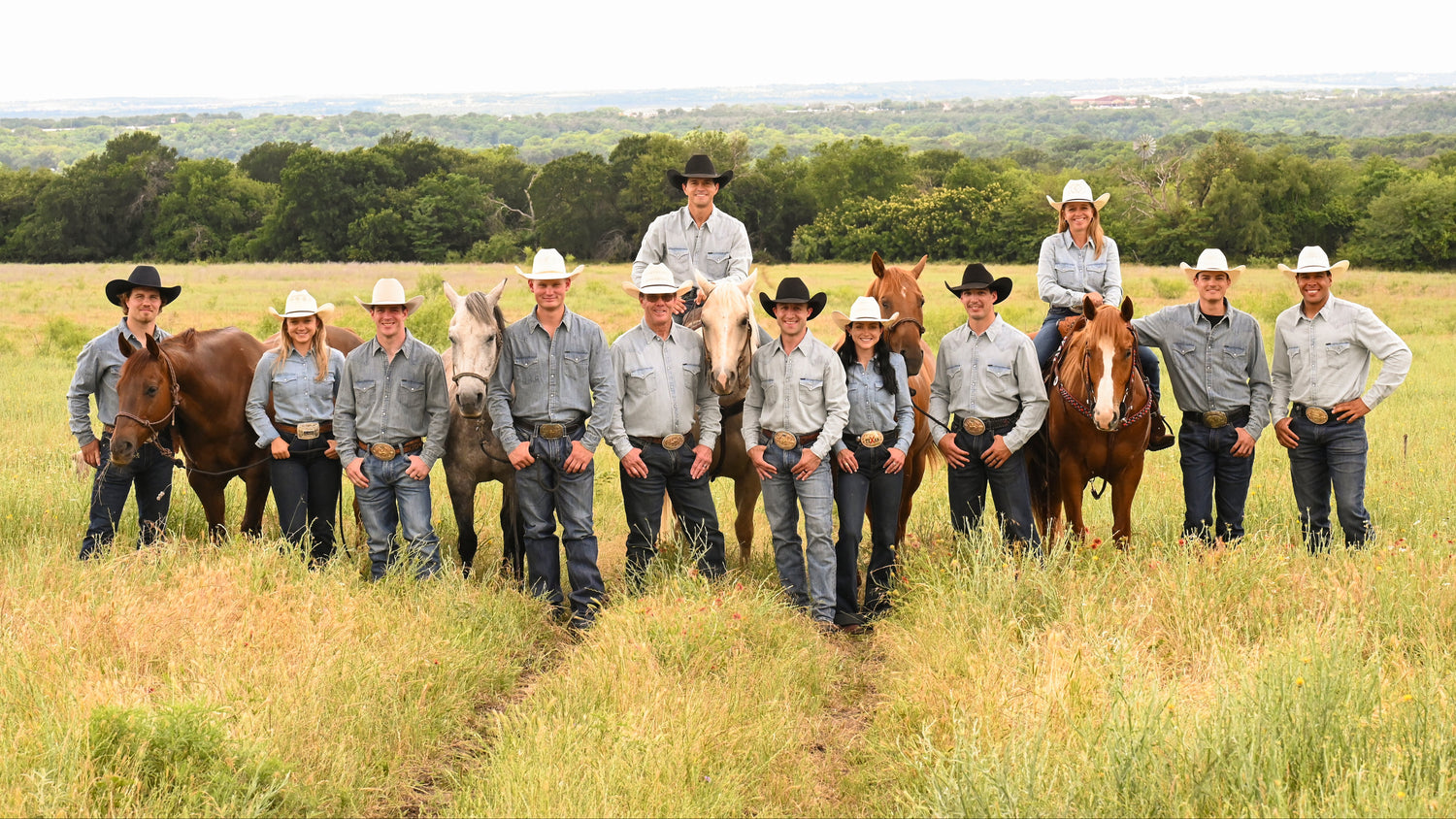 Group of people in cowboy hats and hats with horses in a field