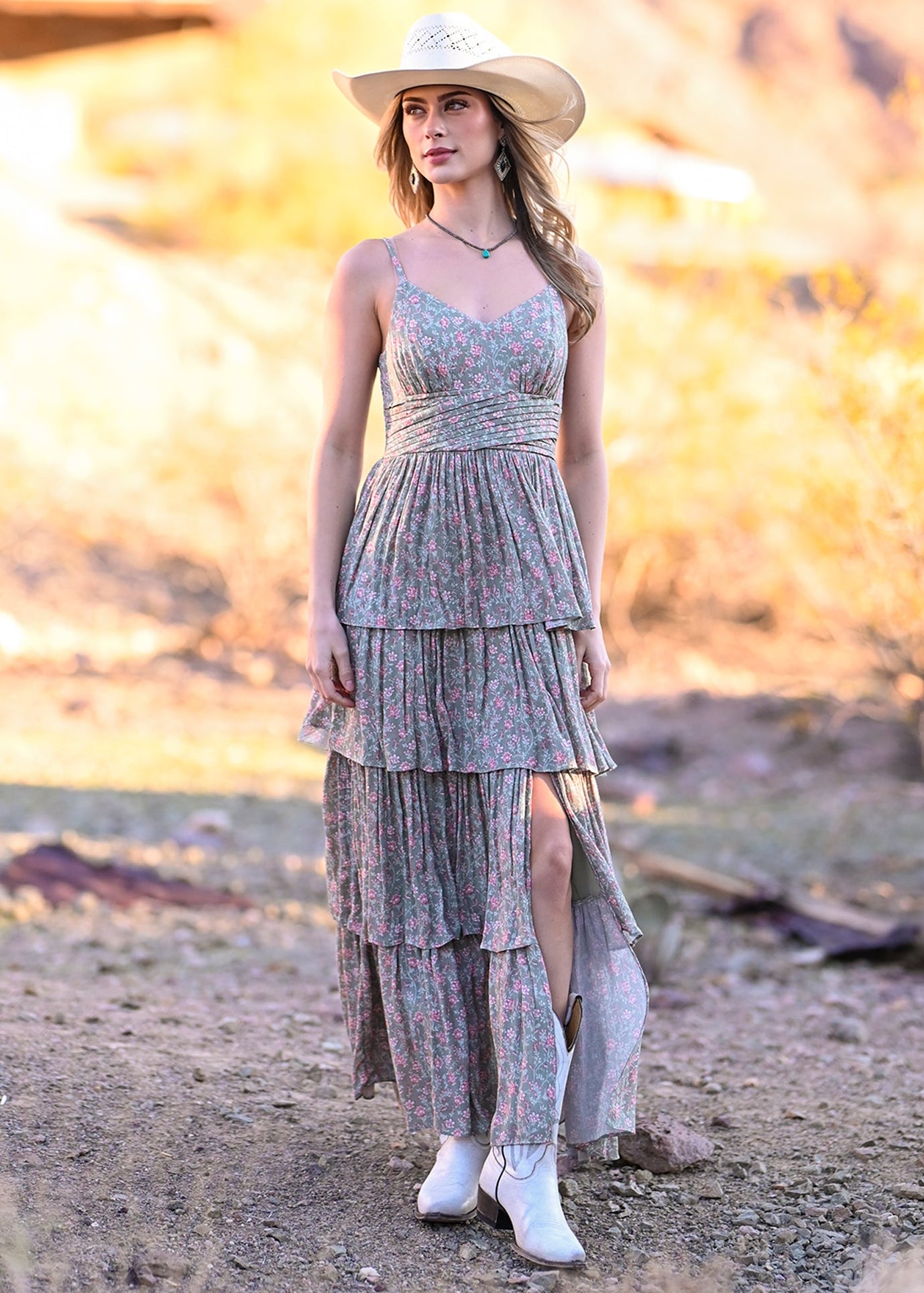 Woman in a layered dress and cowboy hat standing in a desert landscape.