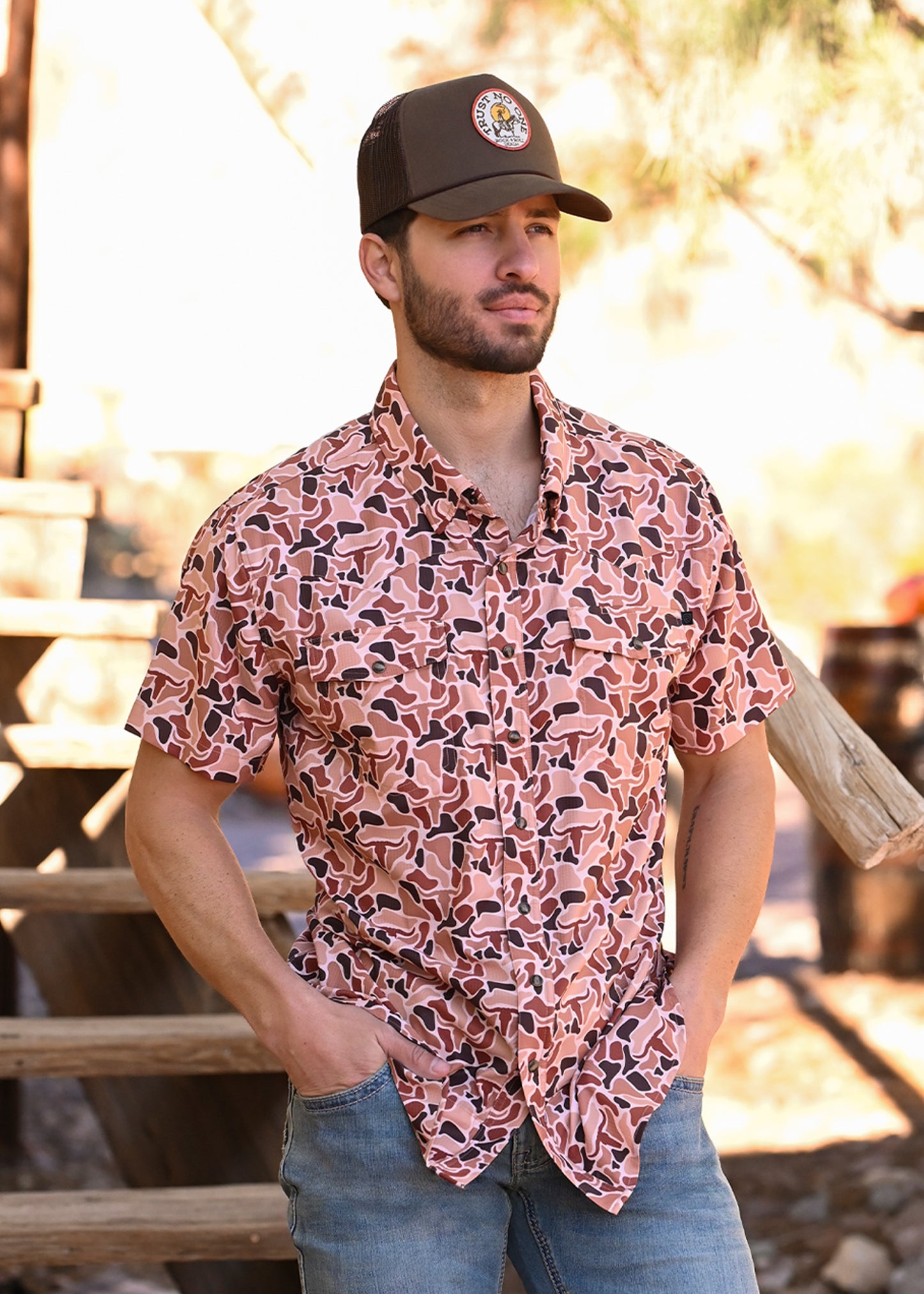 Man wearing a performance shirt that has a camo and steer pattern in orange and brown hues. 