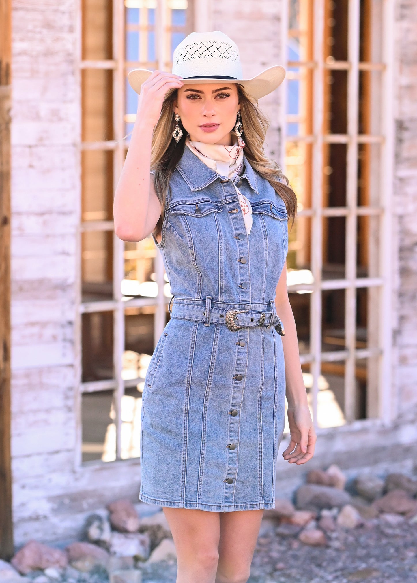 Woman wearing a denim dress and cowboy hat in front of a rustic wooden door.