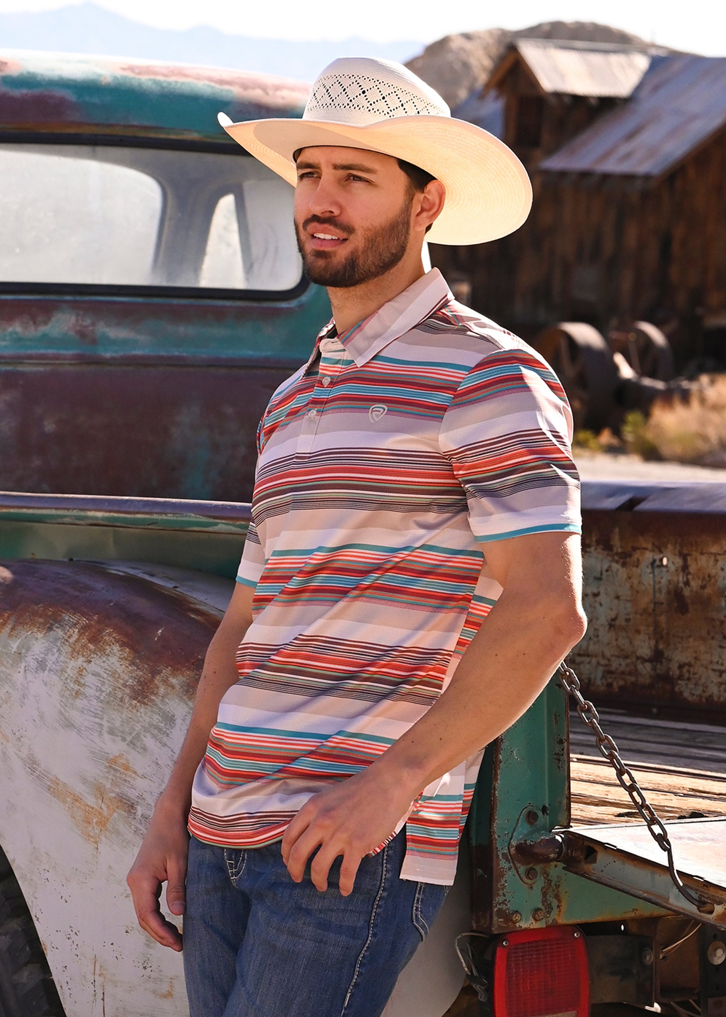 Man wearing a stripe polo leaning up against a vintage truck