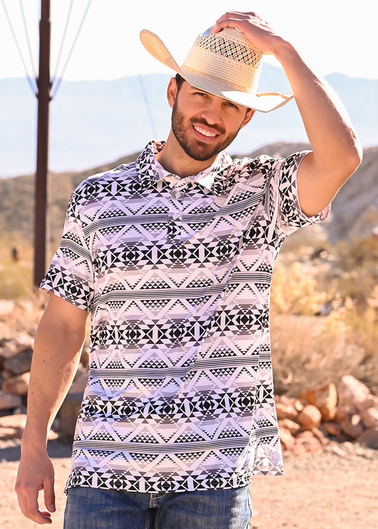 Man wearing an aztec print, black and white polo in a desert setting 