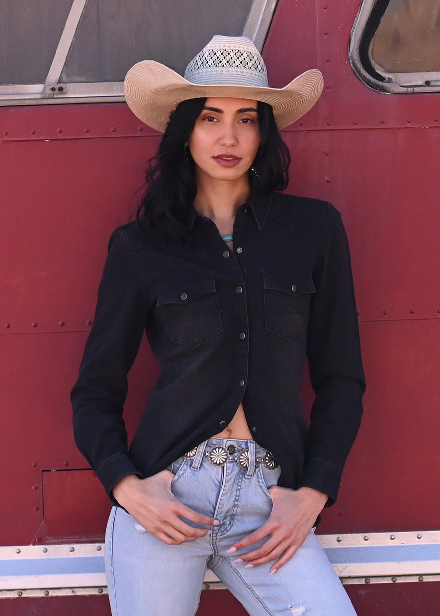 Woman wearing a cowboy hat and black shirt in front of a red vehicle