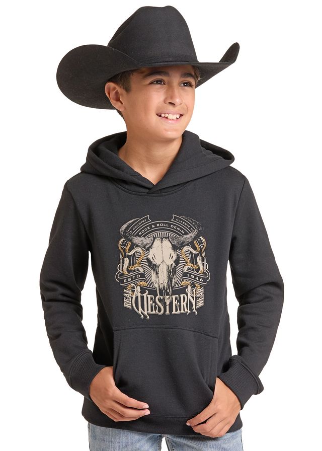 A young boy wearing a black Western-themed hoodie with a large skull and bison graphic on the front, paired with a black cowboy hat and light blue jeans.