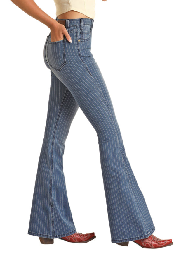 A person in Rock & Roll Denim’s Stripped Blue Button Flare Jeans, a light top, and red cowboy boots stands in side profile with one hand in their pocket.