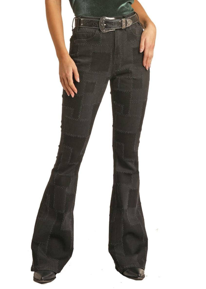 Woman wearing a green top and black bell-bottom pants with a black cowboy hat on a white background