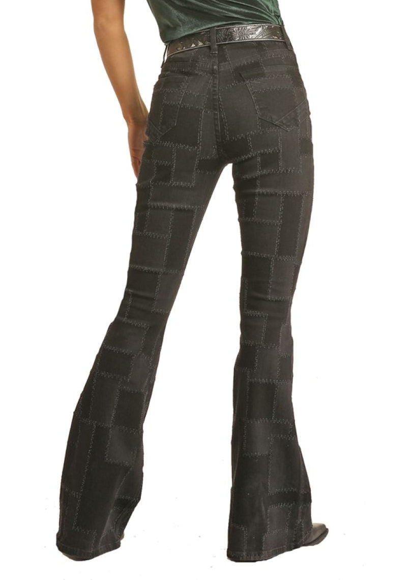 Woman wearing a black cowboy hat, green top, and dark flared jeans on a white background