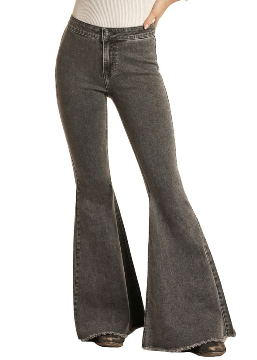 Woman wearing a white long-sleeve top and gray flared jeans with a black cowboy hat on a white background