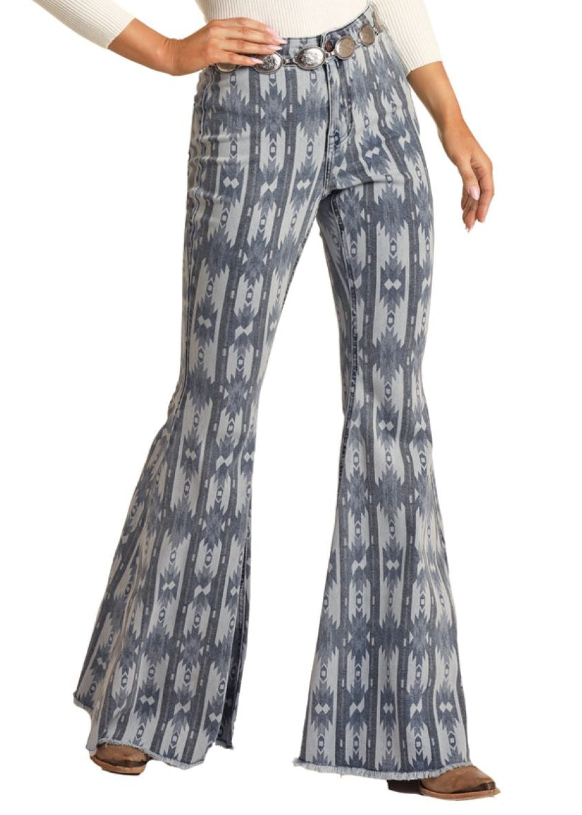 Woman wearing a white long-sleeve top and blue patterned flared pants with a beige cowboy hat on a white background.