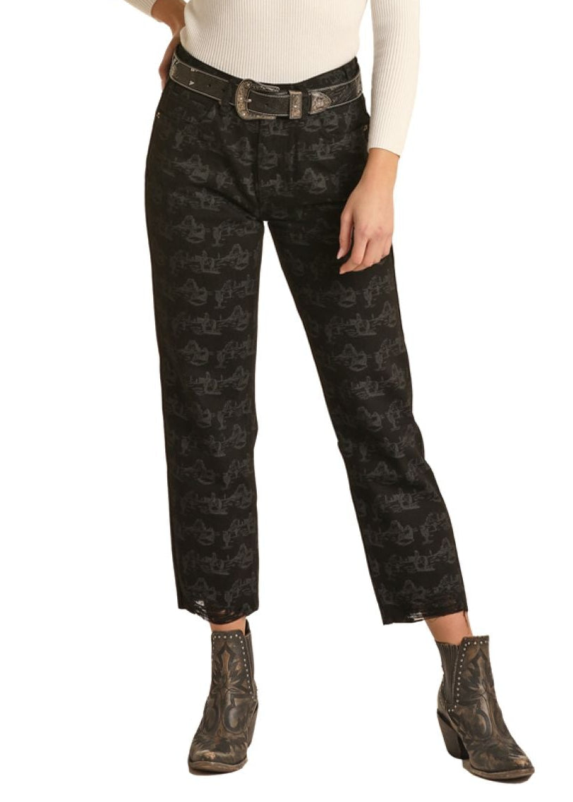 Woman wearing a black cowboy hat, beige top, and black plaid pants on a white background