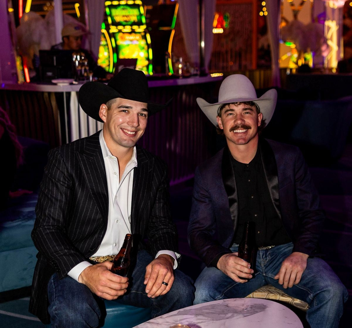 Two men in cowboy hats sitting together in a lively bar setting.